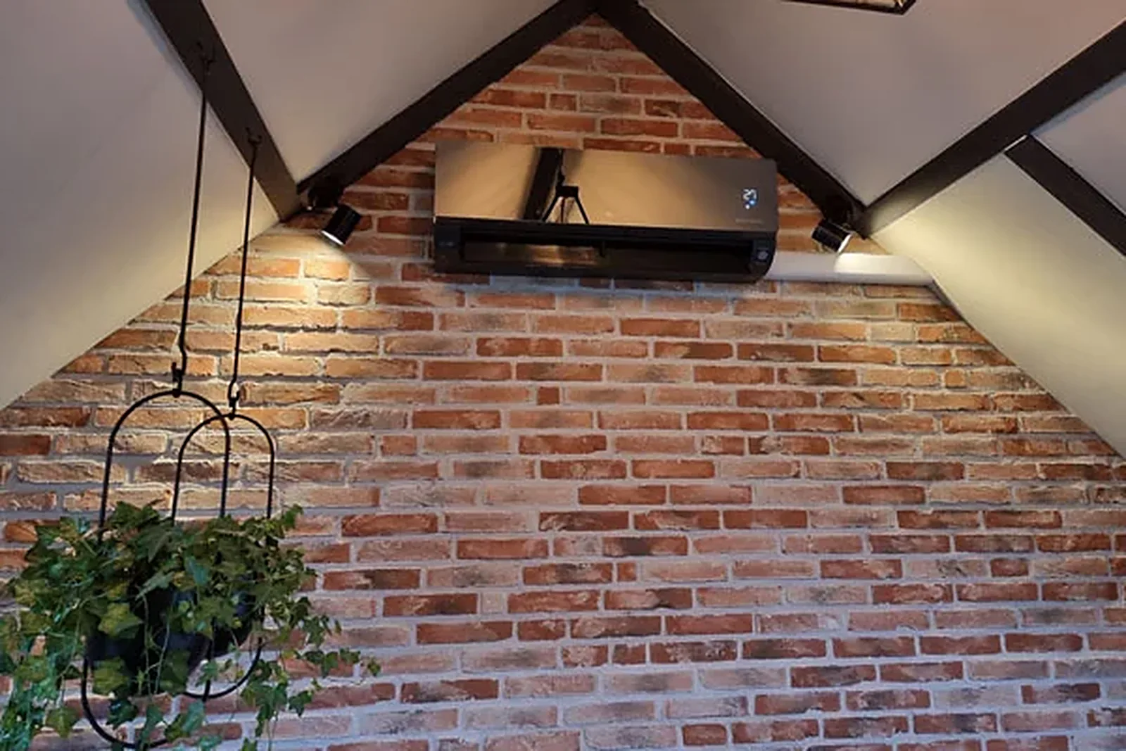 Zwarte airco tegen een bakstenen wand op een zolder